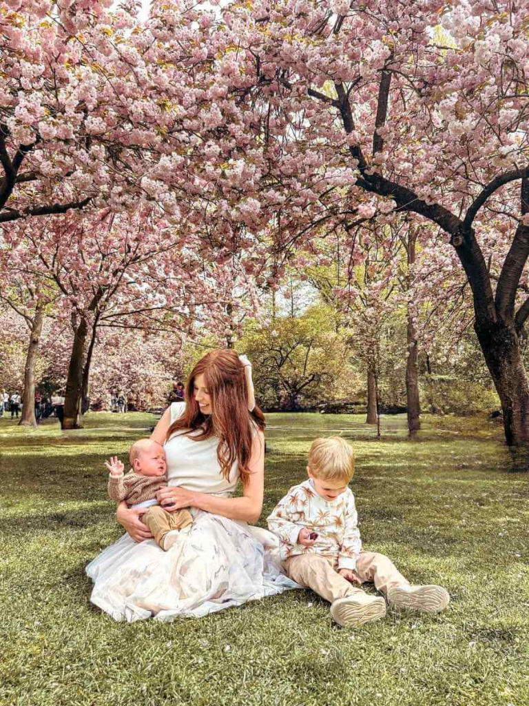 Mum in the City sitting with two toddlers and a baby under cherry blossoms at Brooklyn Botanic Garden