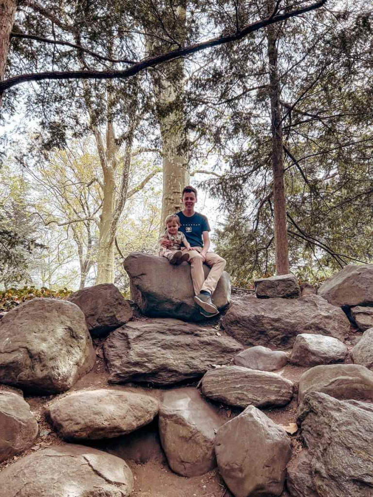 Father and young child climbing on rocks in the natural play area at Brooklyn Botanic Garden