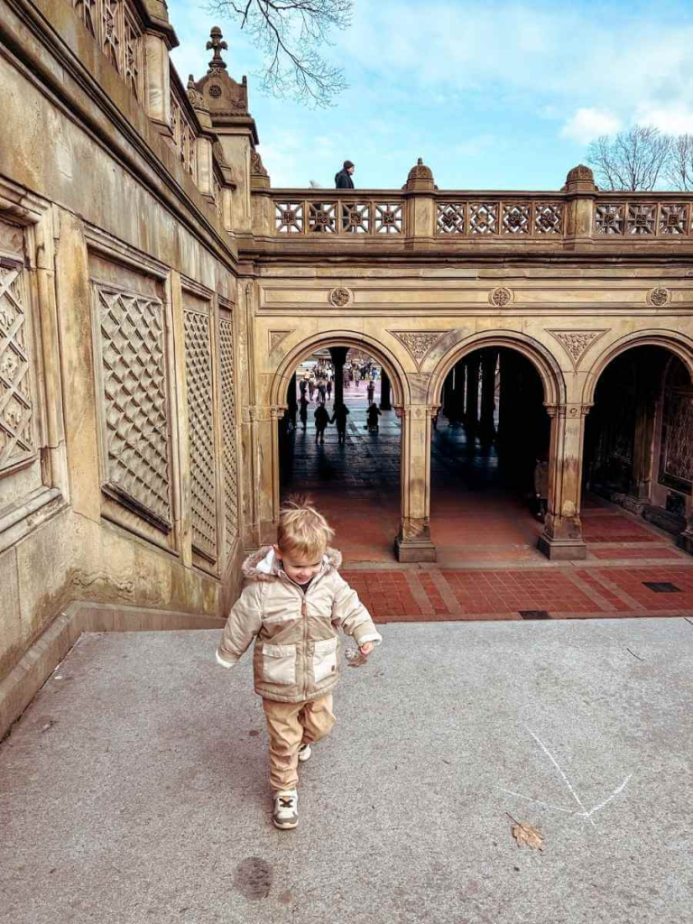 A toddler running up the steps of the Bethesda Terrace, a beautiful spot to visit in Central Park with kids