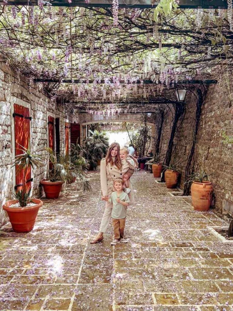 Me with my two sons standing under a purple flower-covered archway at the Budva Citadel