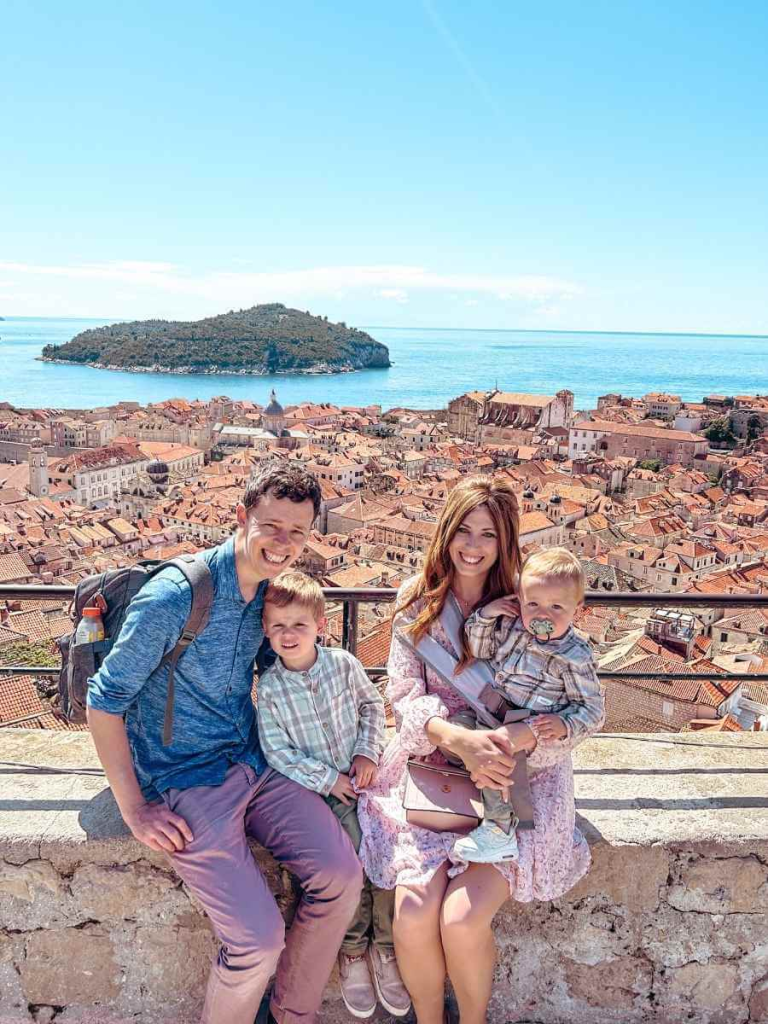 Family smiling on the city walls tith a beautiful view of Dubrovnik in the background.