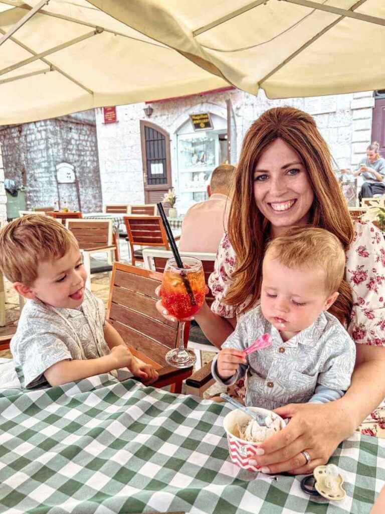 Baby eating ice cream while mum enjoys an Aperol Spritz at a cafe in Kotor with kids.