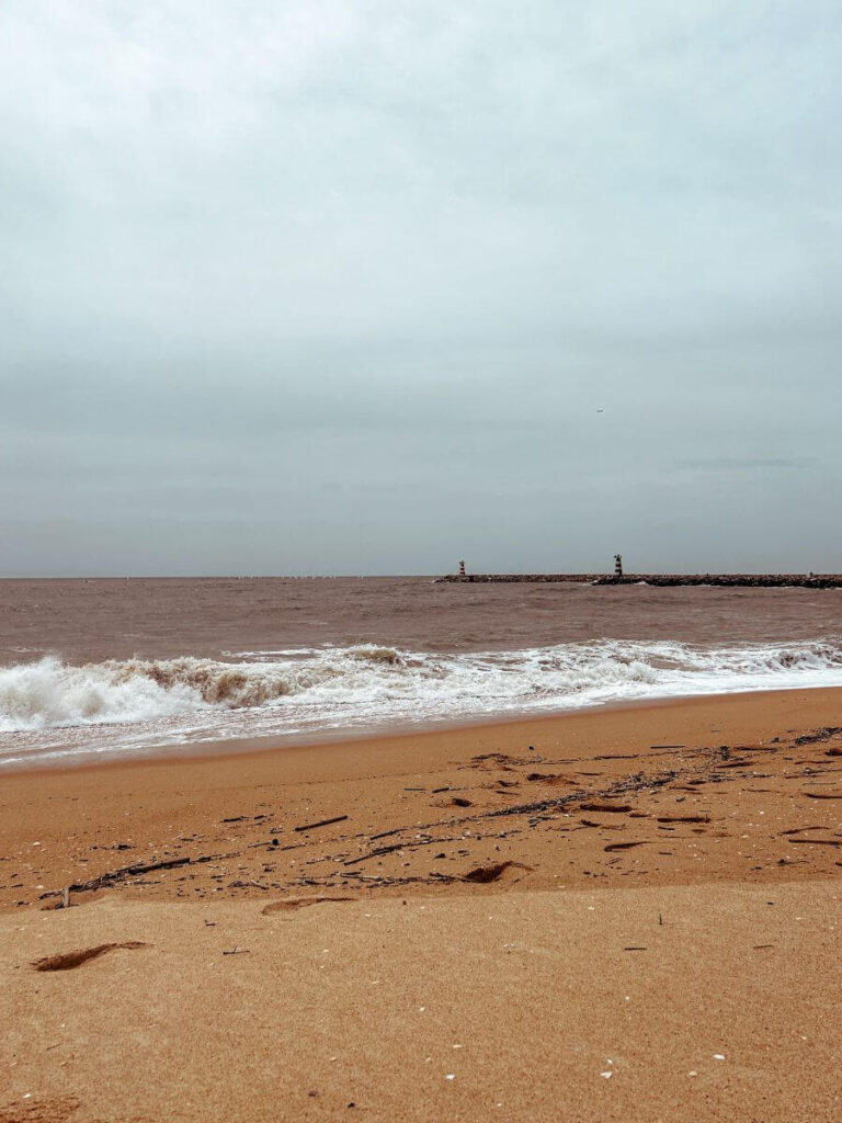 Wide sandy beach in Vilamoura with calm waves and two lighthouses visible in the distance