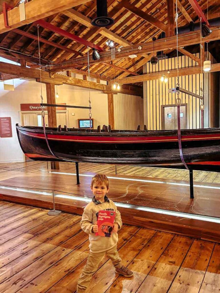 Child completing an activity worksheet by a boat at the Museum of London Docklands