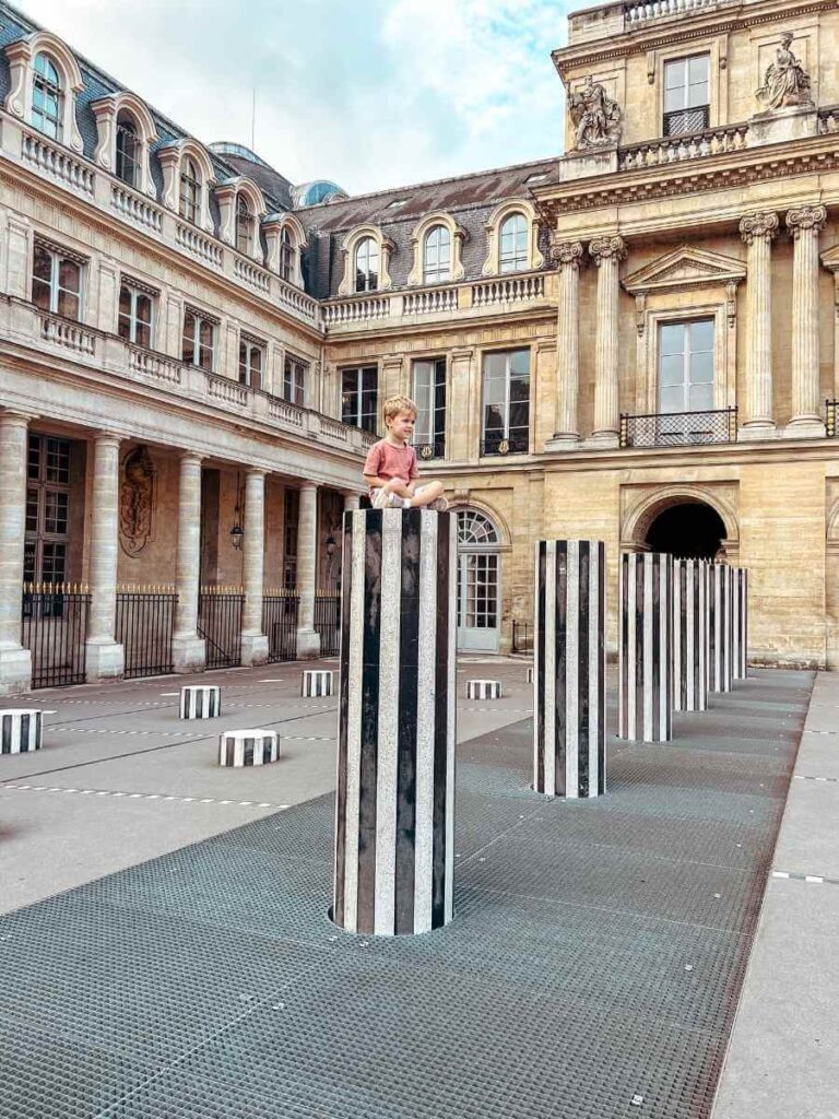 Little boy sitting on a black and white column at the Palais Royal in Paris