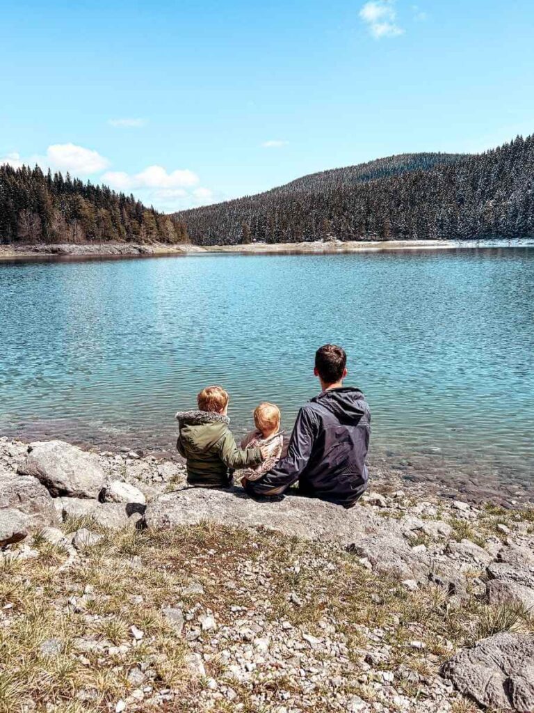 Dad sitting by Black Lake with two young children, enjoying the peaceful nature of Durmitor National Park