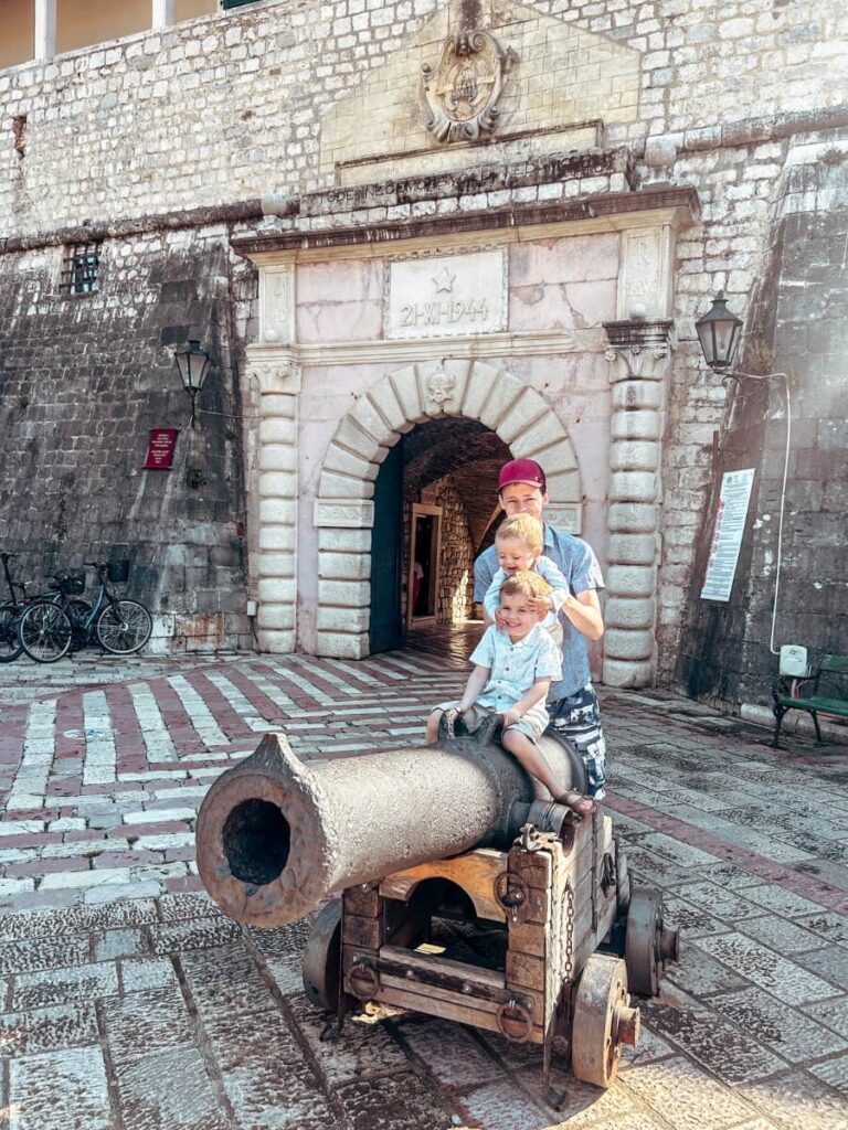 Two young children sitting on a historic cannon outside the walls of Old Town Kotor, Montenegro.