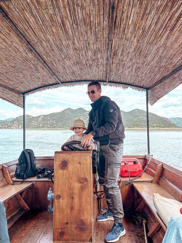 Child driving the boat alongside the captain during a Lake Skadar boat trip