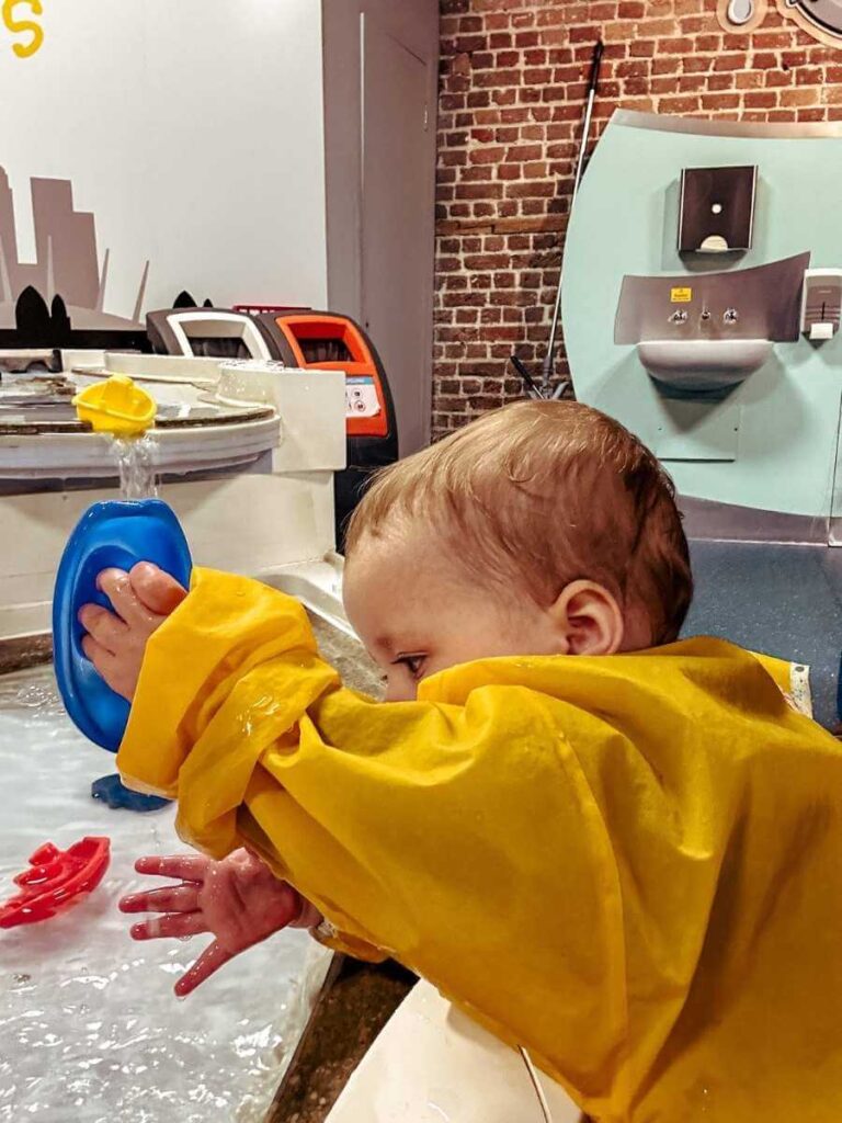 Baby playing at the water table in the Mudlarks soft play area at the Museum of London Docklands.