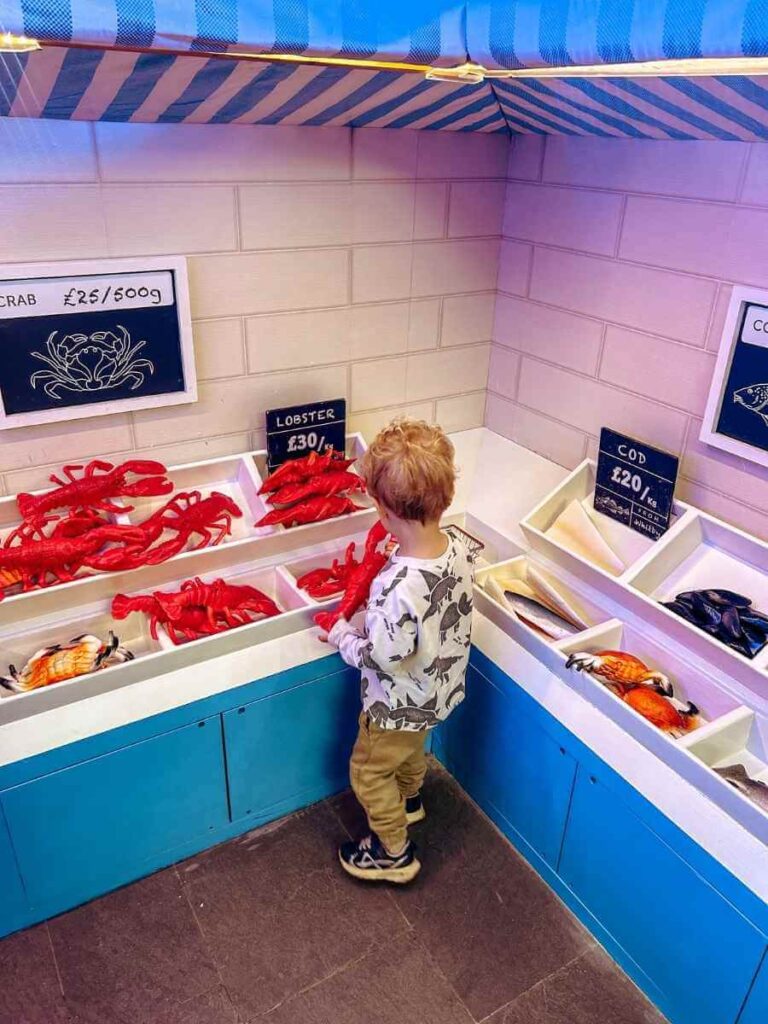 Child playing in the fishmongers role-play area at the Ahoy! Maritime Museum, part of the Greenwich Maritime Museum children's gallery.