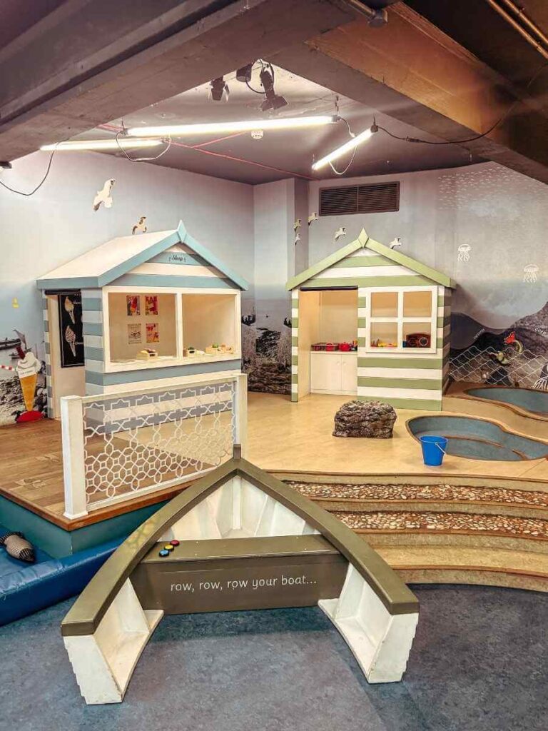 View of the colourful beach huts and boat inside the Ahoy! Maritime Museum kids' play area in Greenwich.