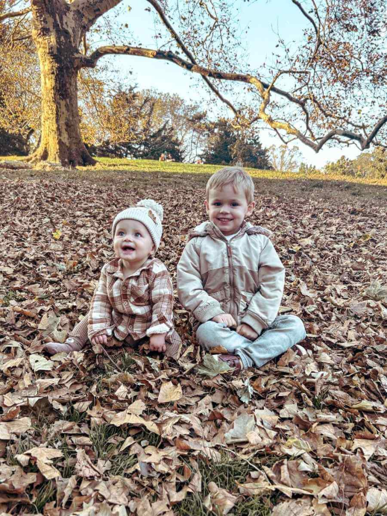 My kids playing in a pile of autumn leaves in Central Park — a must-do family experience in New York City in October.

