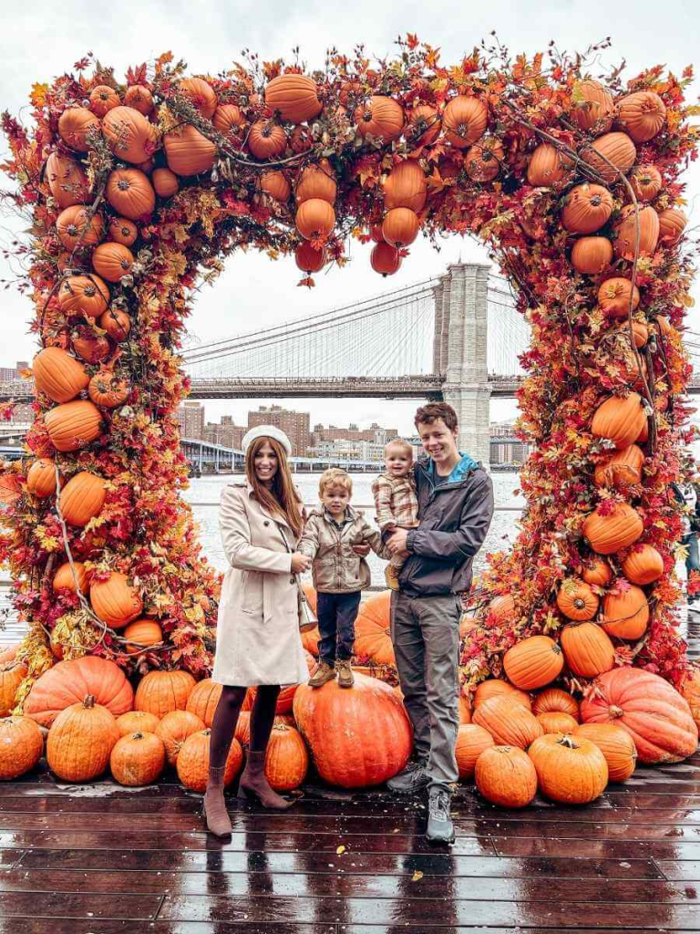 Our family posing under the bright orange pumpkin arch at Pier 17 — a seasonal New York City photo stop in October.

