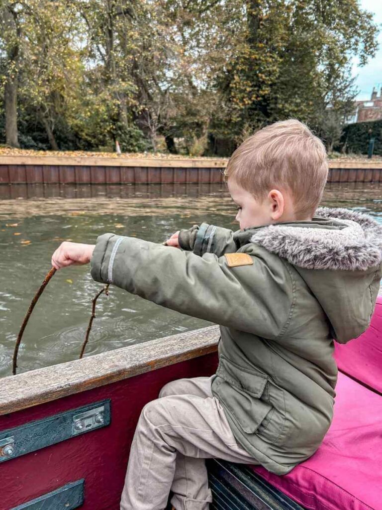 Young child playfully rowing during a relaxed Cambridge punting tour for families.