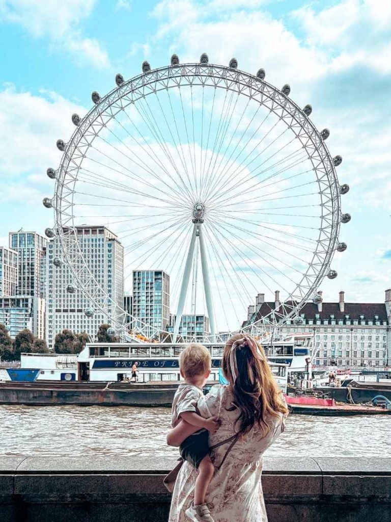 Mum in the City and her baby looking at the view of the London Eye from across the river Thames.
