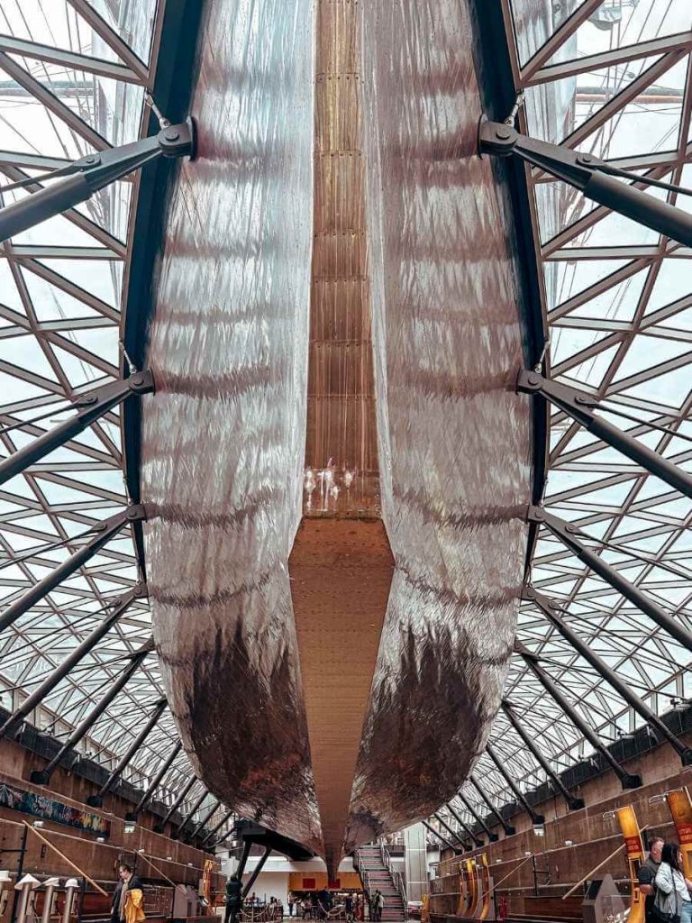 View from beneath the Cutty Sark, showcasing the impressive golden hull and supporting structure.