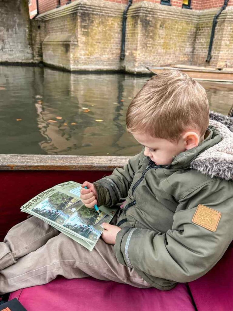 Child completing a Cambridge punting tour activity book during a family day out.