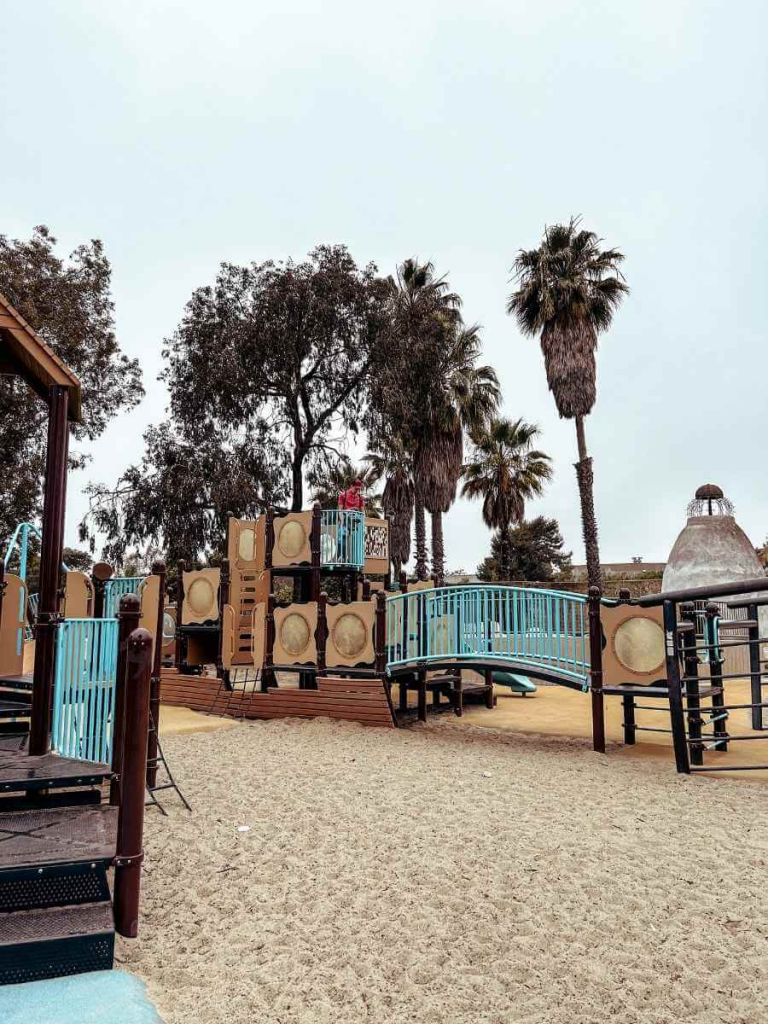 Shipwreck-themed climbing structure at Chase Palm Park playground in Santa Barbara, with palm trees and ocean views nearby.