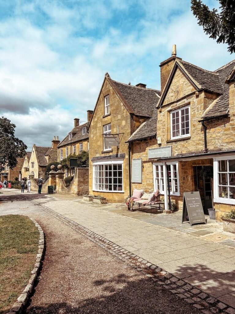 View of Broadway high Street, full of honey stone buildings, shops and cafes. A mist visit town to add to your 2 day Cotswold itinerary. 