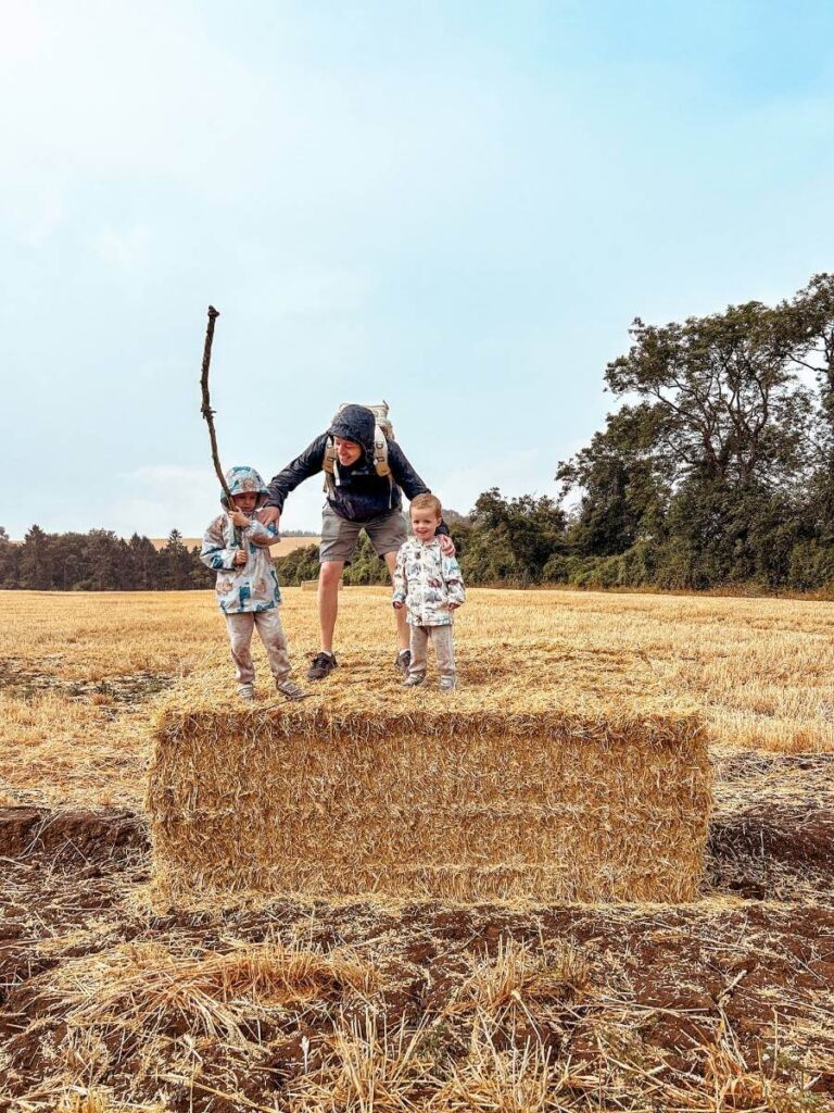 Kids and Dad climbing on a hay bale during a family hike in the Cotswolds countryside