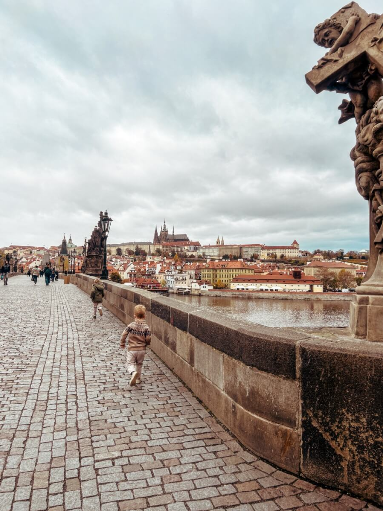 Kids running across Charles Bridge with a view of Prague Castle in the background.